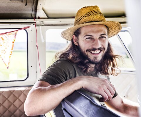 Ein Mann sitzt auf dem Fahrersitz in einem Van und trägt einen Strohhut.