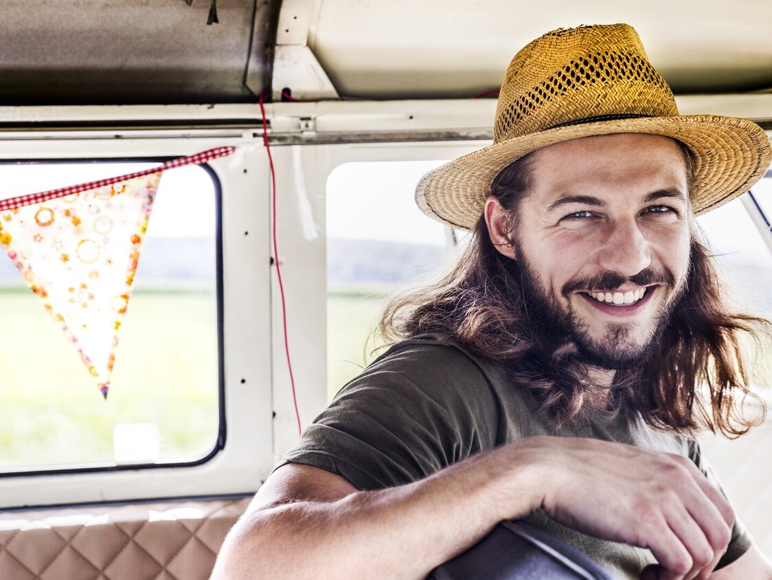 Ein Mann sitzt auf dem Fahrersitz in einem Van und trägt einen Strohhut.