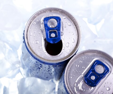 Zwei Getränkedosen, eine geöffnet und eine ungeöffnet, stehen in einer Schicht Eiswürfel.