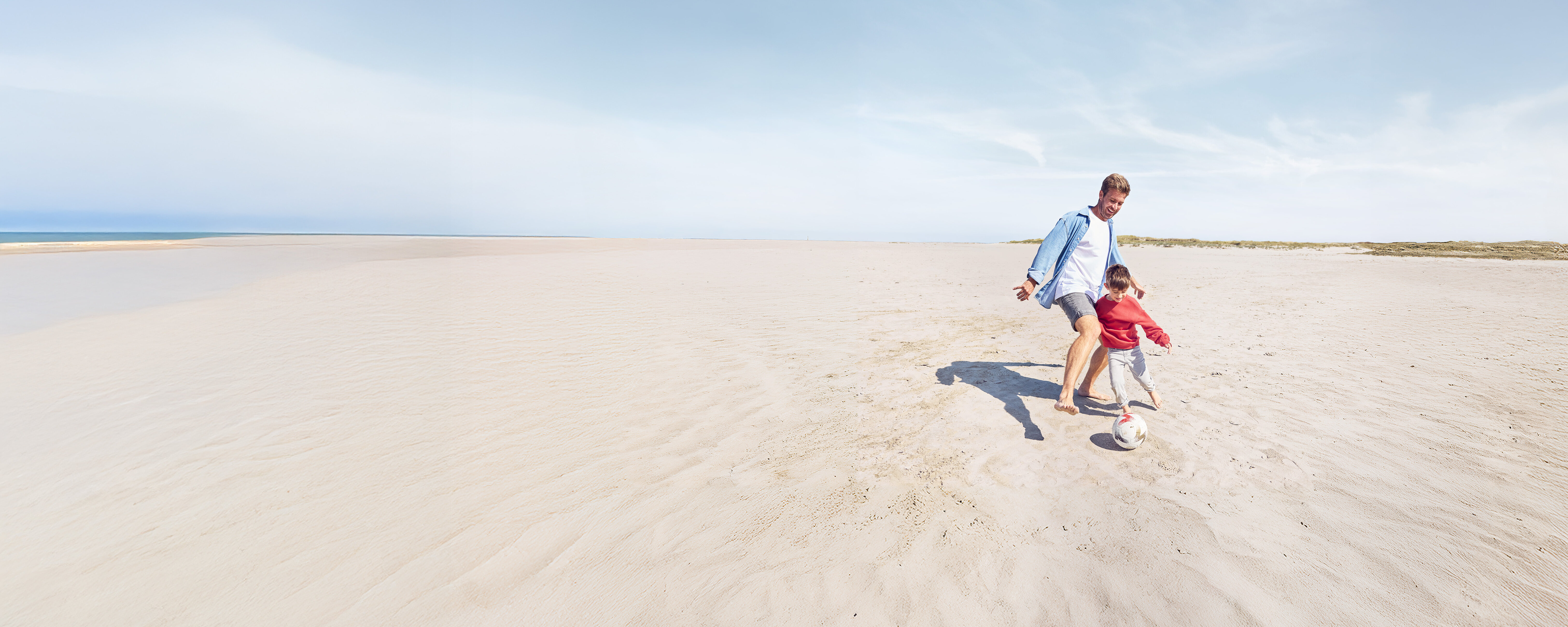 Ein Mann spielt mit seinem Sohn am Strand Fußball.