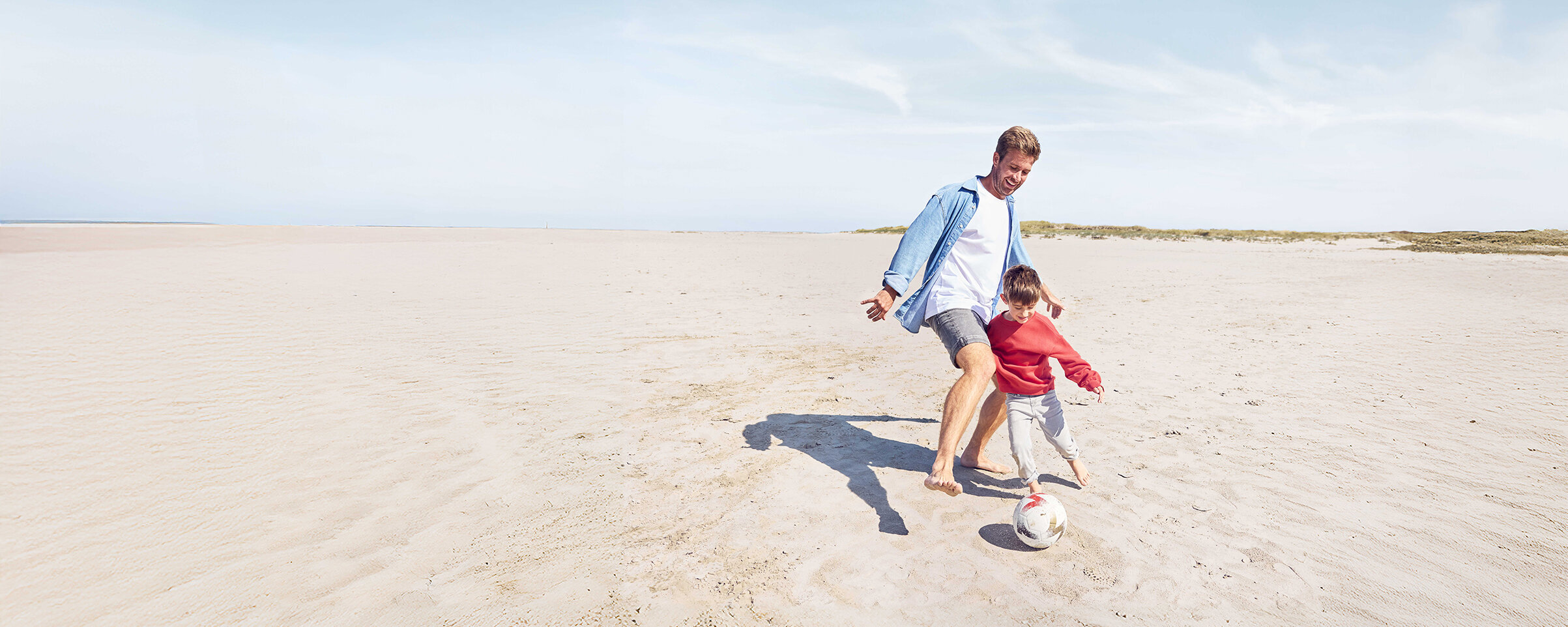 Ein Mann spielt mit seinem Sohn am Strand Fußball.