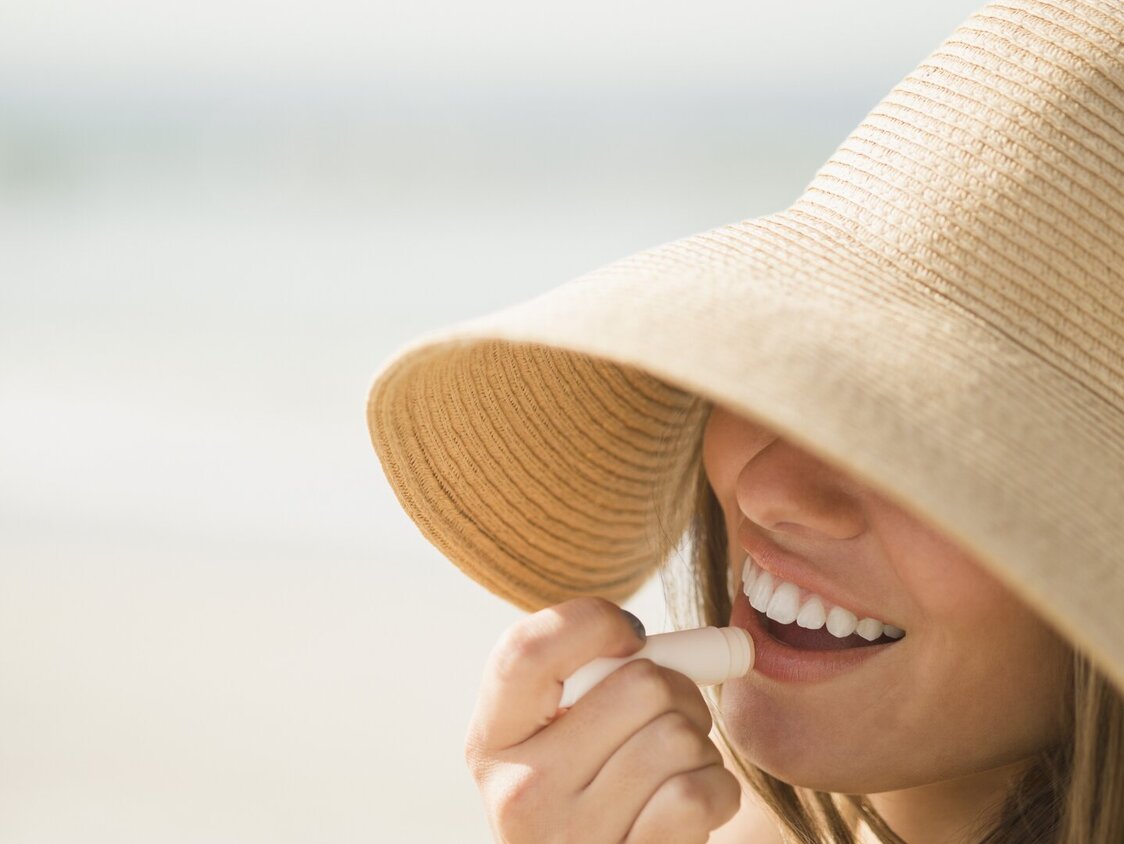 Frau mit Sonnenhut trägt Sonnenschutz auf Ihren Mund auf.