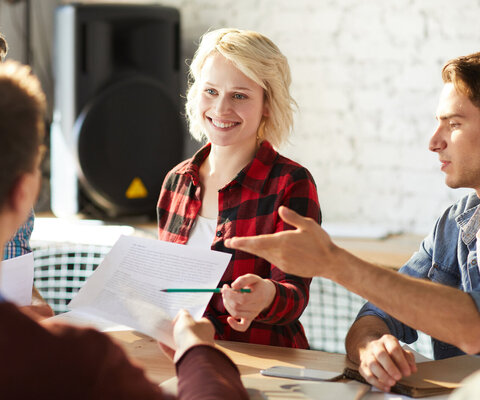 Drei Männer und zwei Frauen sitzen im Büro an einem Tisch zusammen und diskutieren Ideen.