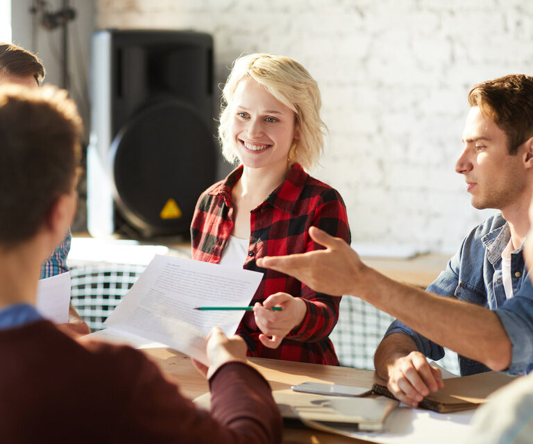 Drei Männer und zwei Frauen sitzen im Büro an einem Tisch zusammen und diskutieren Ideen.