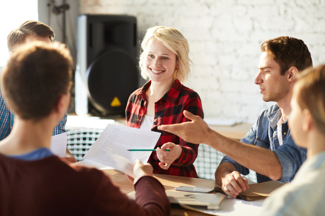 Drei Männer und zwei Frauen sitzen im Büro an einem Tisch zusammen und diskutieren Ideen.