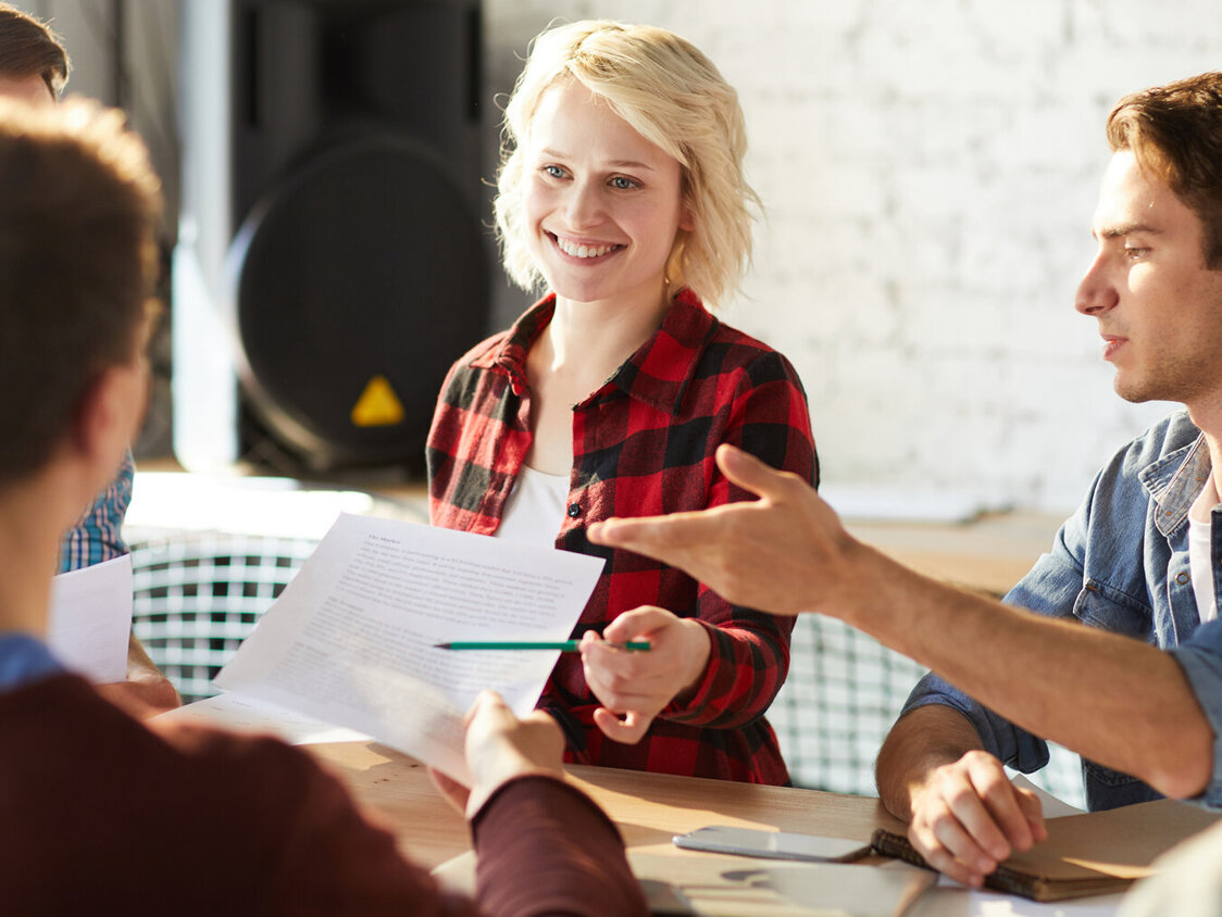 Drei Männer und zwei Frauen sitzen im Büro an einem Tisch zusammen und diskutieren Ideen.