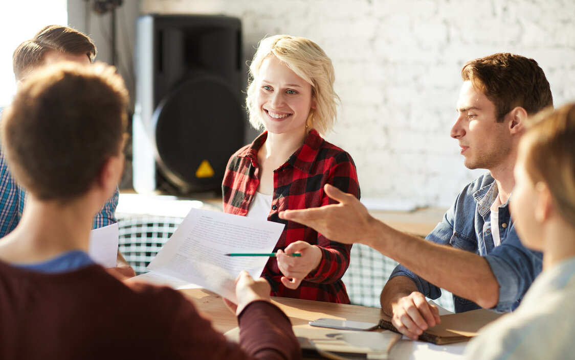 Drei Männer und zwei Frauen sitzen im Büro an einem Tisch zusammen und diskutieren Ideen.