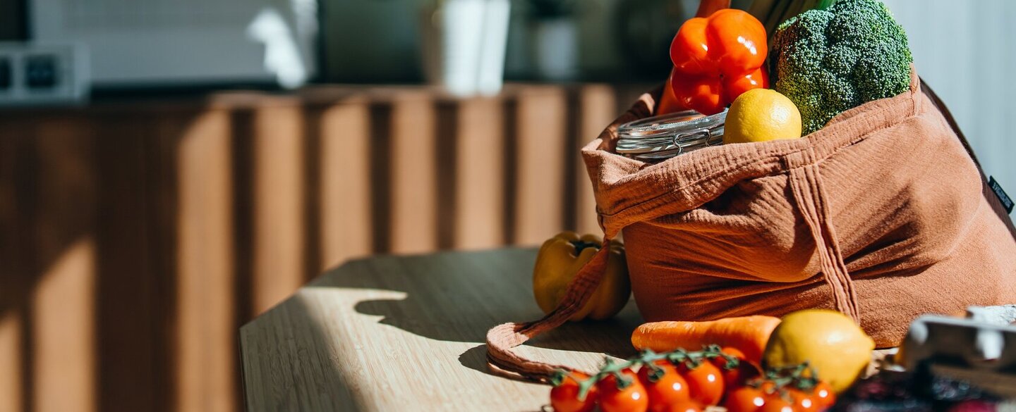 Auf einem Tisch steht eine Einkaufstasche, die mit verschiedenen Gemüsesorten gefüllt ist.