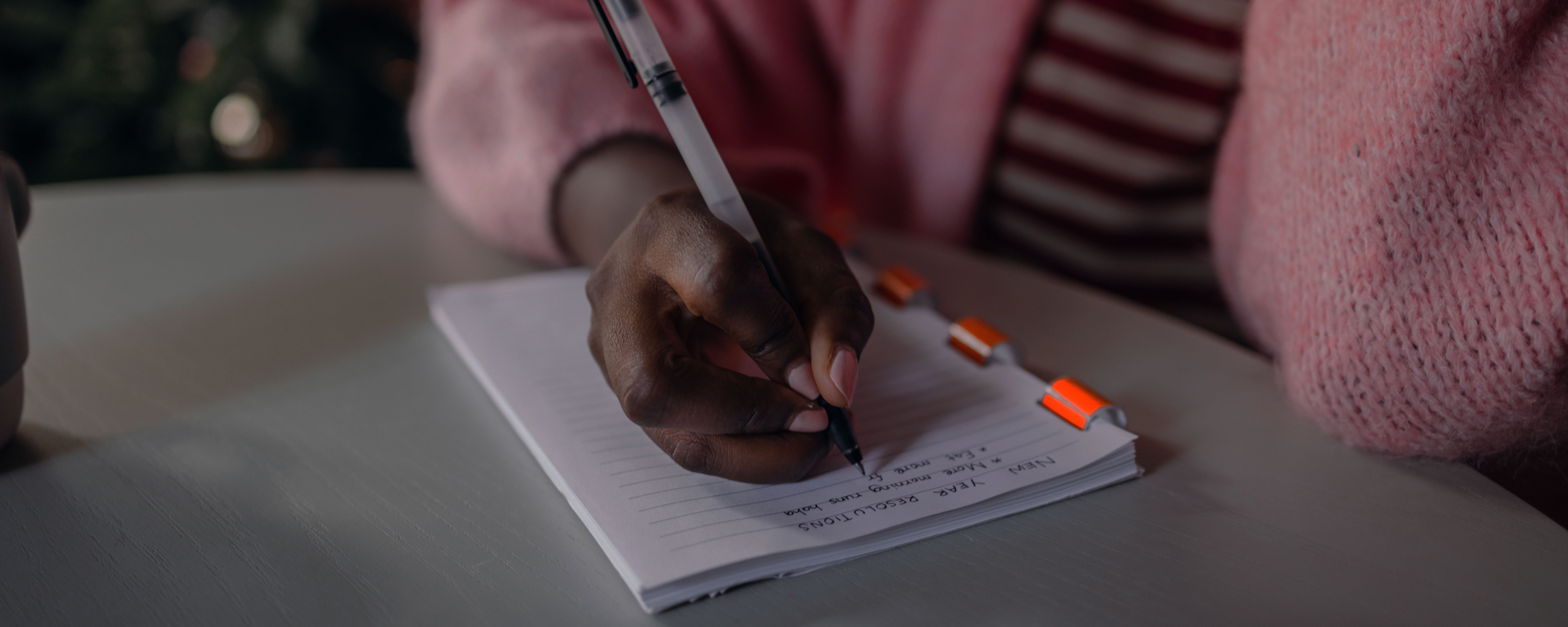 Eine Frau in einer rosa Strickjacke schreibt Neujahrsvorsätze auf einen Block.