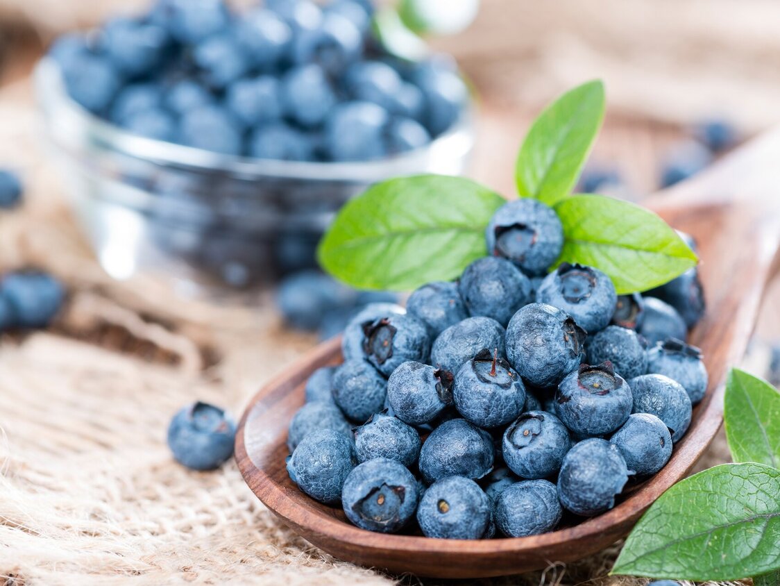 Heidelbeeren liegen auf einem Holzlöffel und in einer Glasschale.