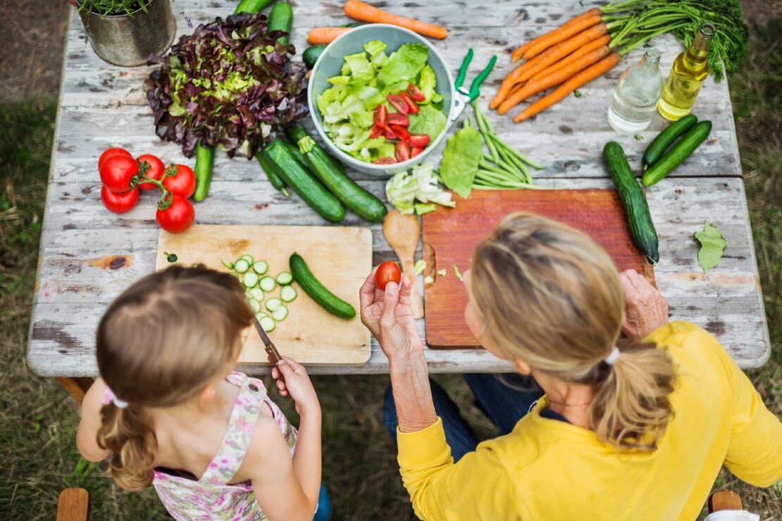Mutter und Tochter bereiten im Garten Salat zu.