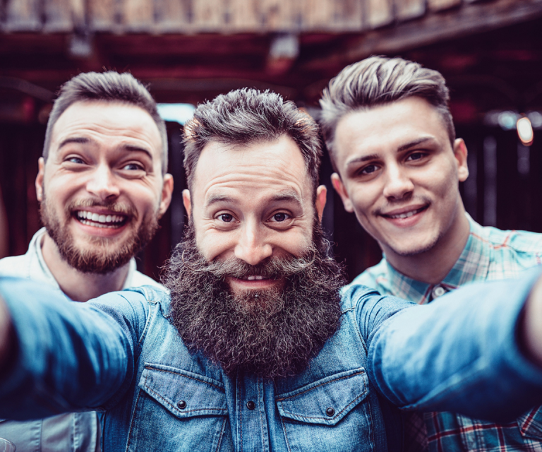 Drei Männer mit Bart und Schnauz die freudig in die Kamera schauen und für den Movember motivieren