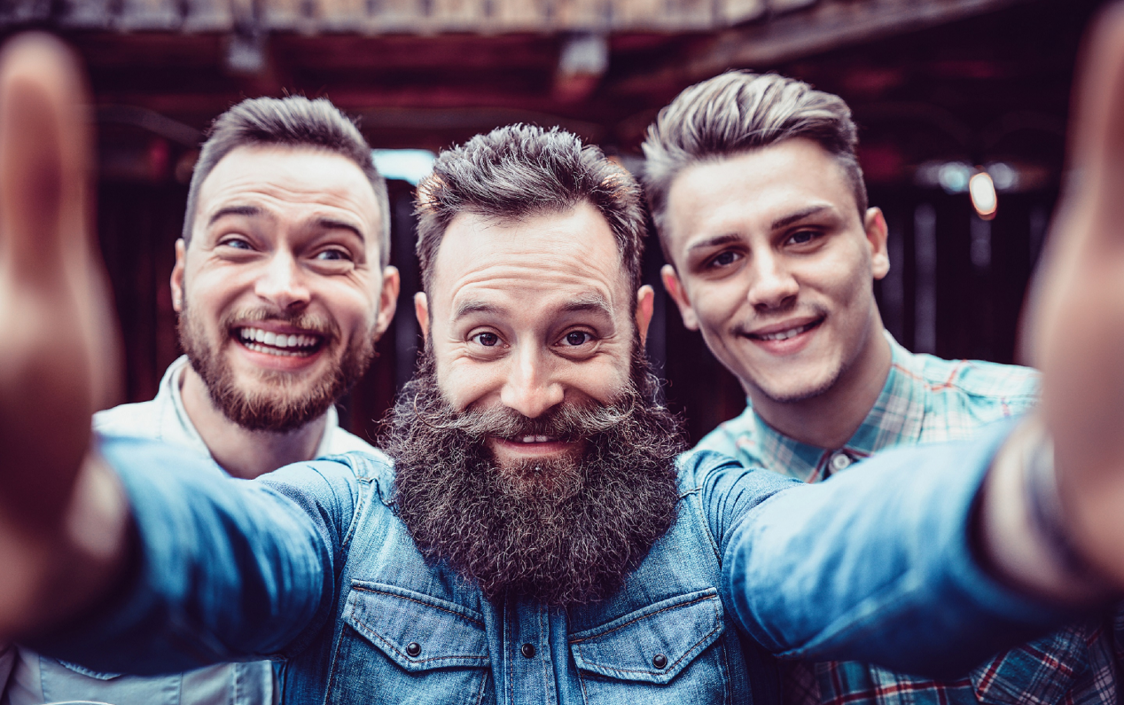 Drei Männer mit Bart und Schnauz die freudig in die Kamera schauen und für den Movember motivieren