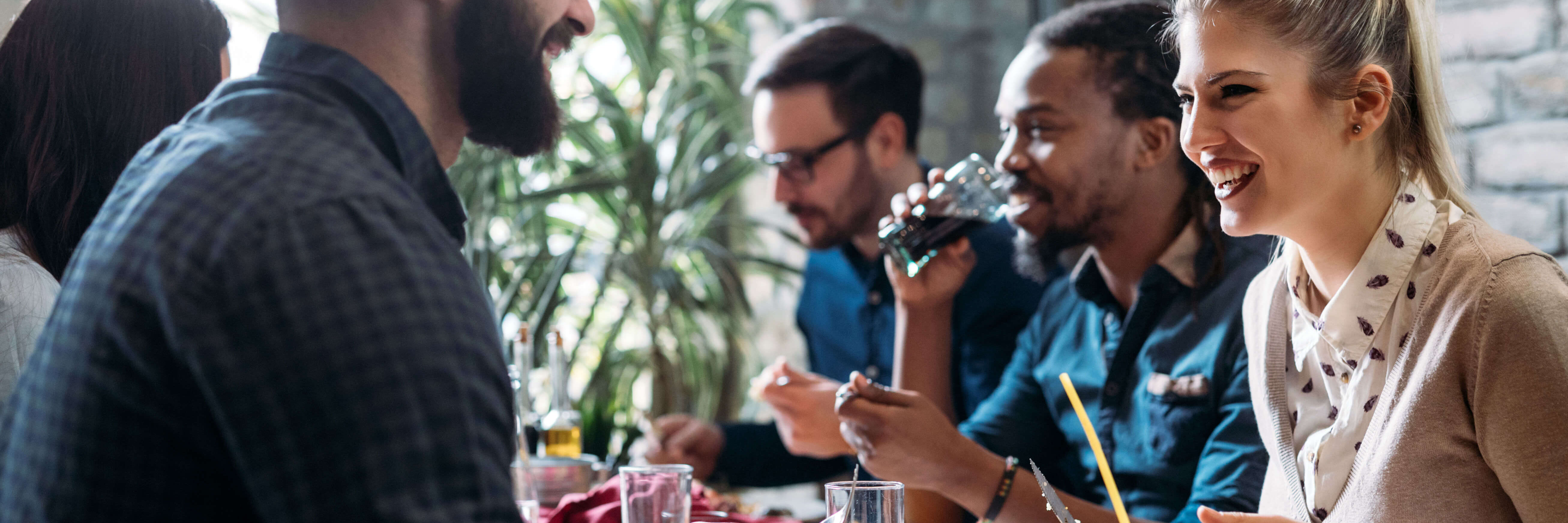 Eine Gruppe von Menschen an einem Tisch in einem Restaurant oder Café. Sie essen, trinken und unterhalten sich lachend.