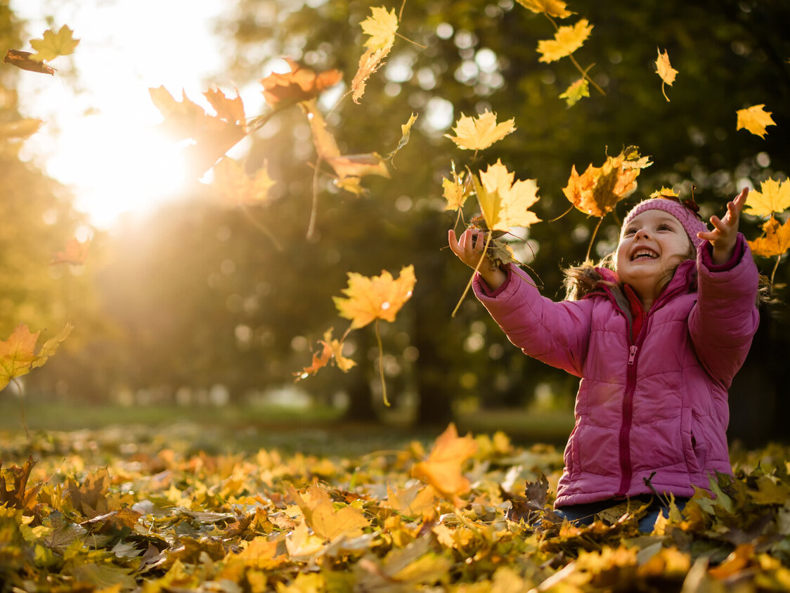 Kind mit pinker Jacke spielt im goldgelbem Laub.
