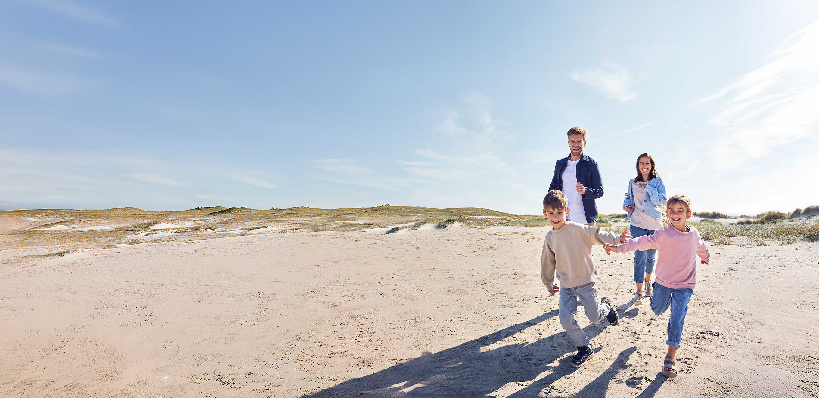 Eine Familie mit zwei Kinder läuft zusammen am Strand.