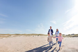 Eine Familie mit zwei Kinder läuft zusammen am Strand.