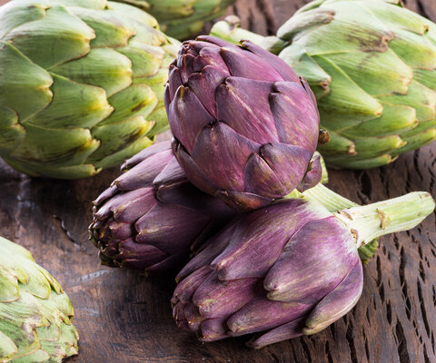 Drei violette und drei grüne Artischocken auf einem hölzernen Untergrund.