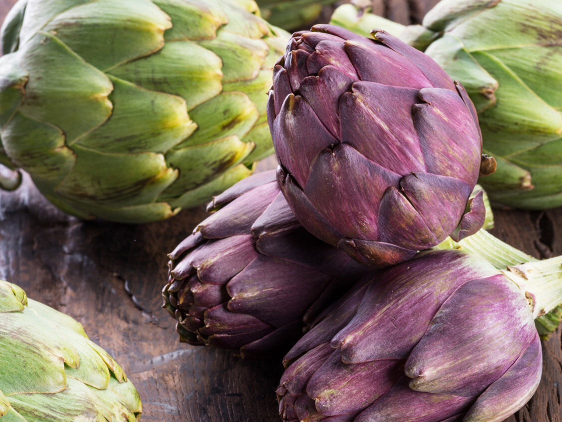 Drei violette und drei grüne Artischocken auf einem hölzernen Untergrund.