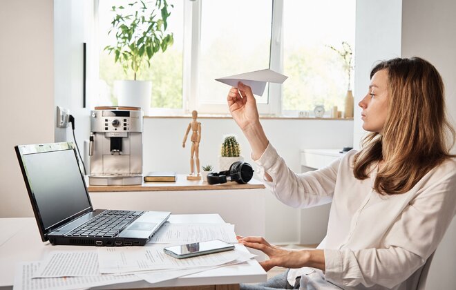 Eine Frau sitzt vor einem Laptop und hat einen Papierflieger in der Hand.