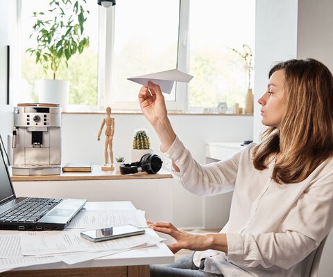 Eine Frau sitzt vor einem Laptop und hat einen Papierflieger in der Hand.