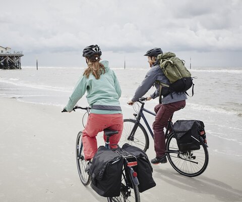 Ein Mann und eine Frauen fahren am Strand Fahrrad und haben viel Gepäck dabei.