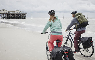 Ein Mann und eine Frauen fahren am Strand Fahrrad und haben viel Gepäck dabei.