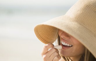 Frau mit Sonnenhut trägt Sonnenschutz auf Ihren Mund auf.