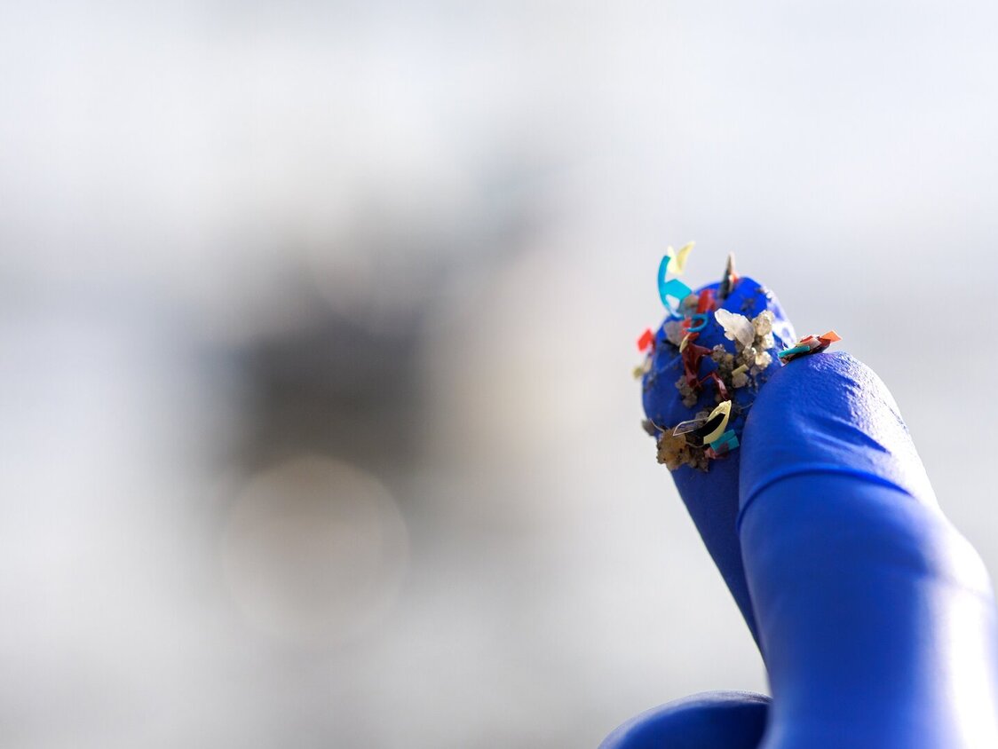 Eine behandschuhte Hand hält zwischen Zeigefinger und Daumen kleine Plastikstückchen.