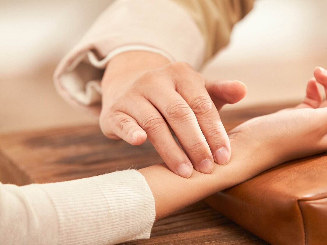 Jemand fühlt mit drei Fingern den Puls einer anderen Person. Es sind nur die Hände zu sehen.