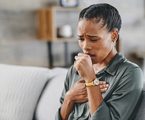 Frau sitzt hustend auf dem Sofa