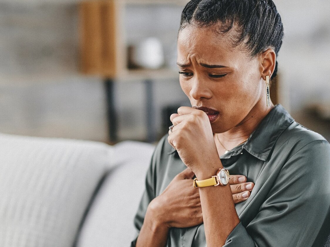 Frau sitzt hustend auf dem Sofa