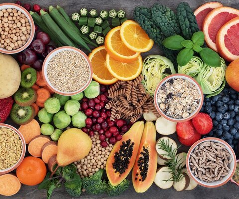  Aufnahme von oben. Auf einem Tisch liegen gesunde Lebensmittel: Obst, Vollkornnudeln, Nüsse, Blaubeeren, Apfel, Orangen, Kiwi, Erdbeeren, Birne, Melone, Pflaume, Brokkoli, Mandarine, Grapefruit, Rosenkohl.