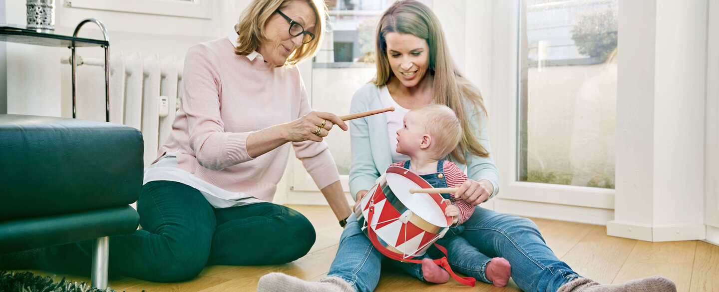 Oma, Mutter und Tochter sitzen auf dem Boden und trommeln.