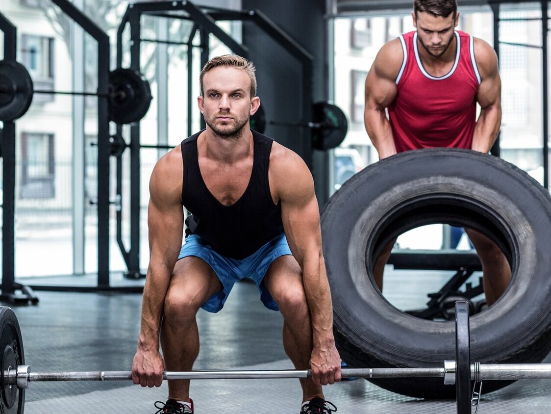 Ein Mann hebt eine Langhantel, ein anderer einen Reifen und eine Frau macht eine Kniebeuge auf einer Box.