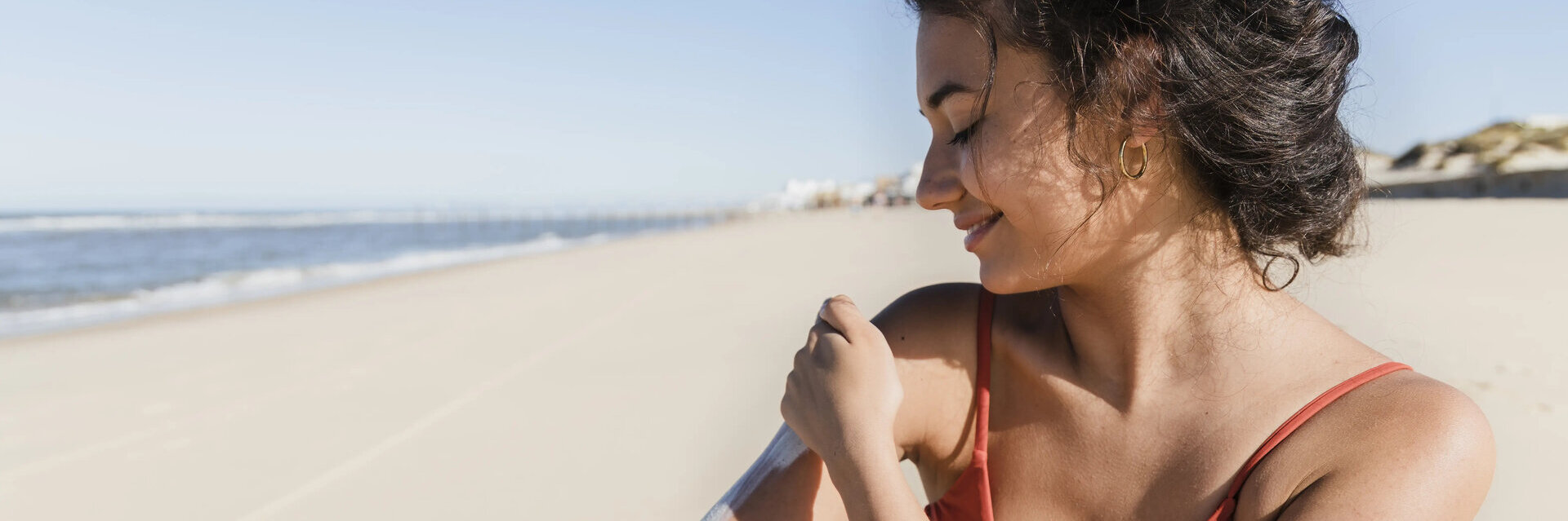 Frau am Strand trägt Sonnencreme auf den Körper auf.