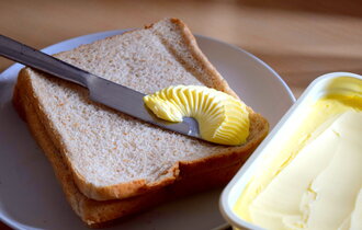 Eine offene Packung Magarine steht neben einem Toastbrot. Auf dem Toast liegt ein Messer mit Butter.