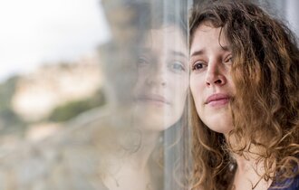 Eine traurige Frau lehnt an einem Fenster