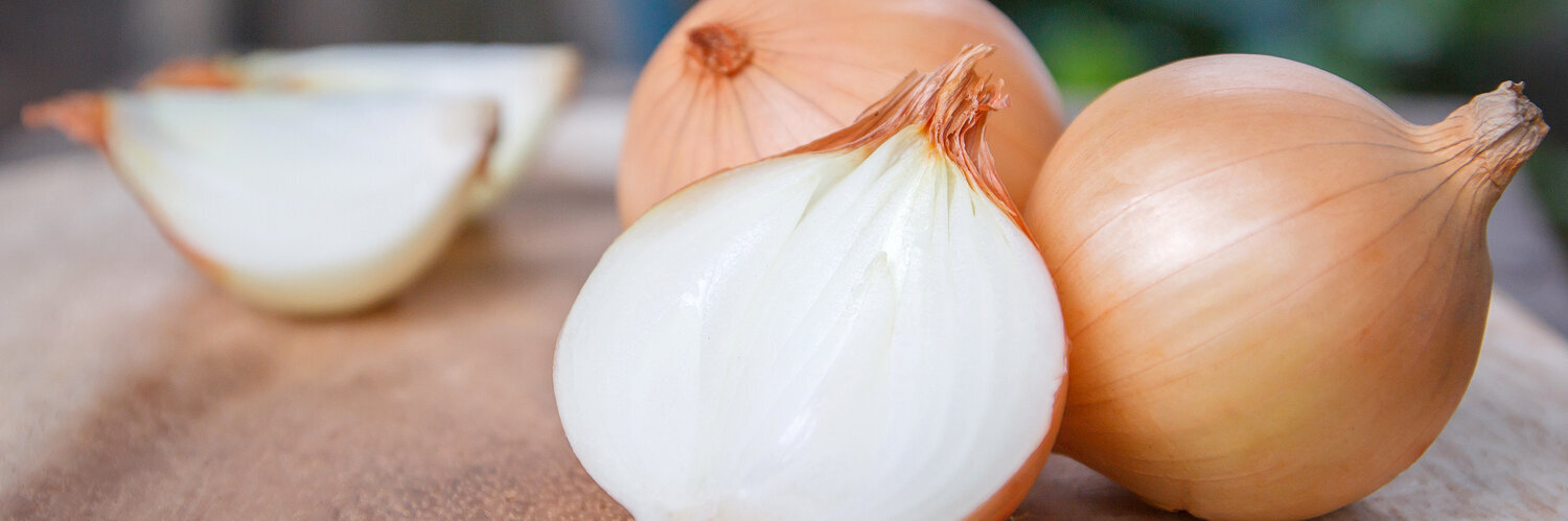 Zwiebelknollen, eine davon aufgeschnitten im Vordergrund.