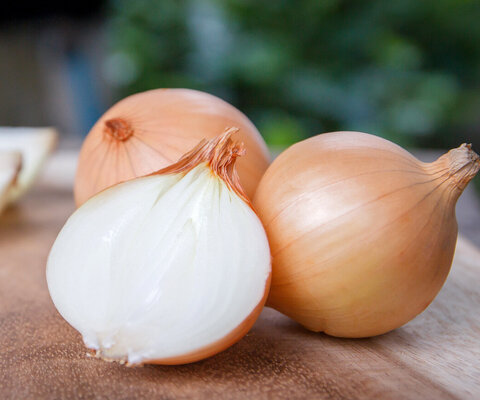 Zwiebelknollen, eine davon aufgeschnitten im Vordergrund.