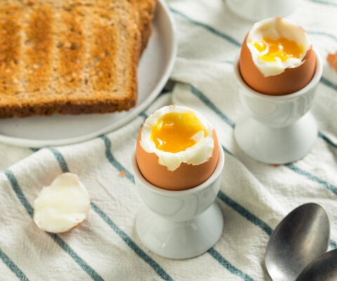 Zwei weichgekochte Eier in Eierbechern, daneben eine Scheibe Toast.