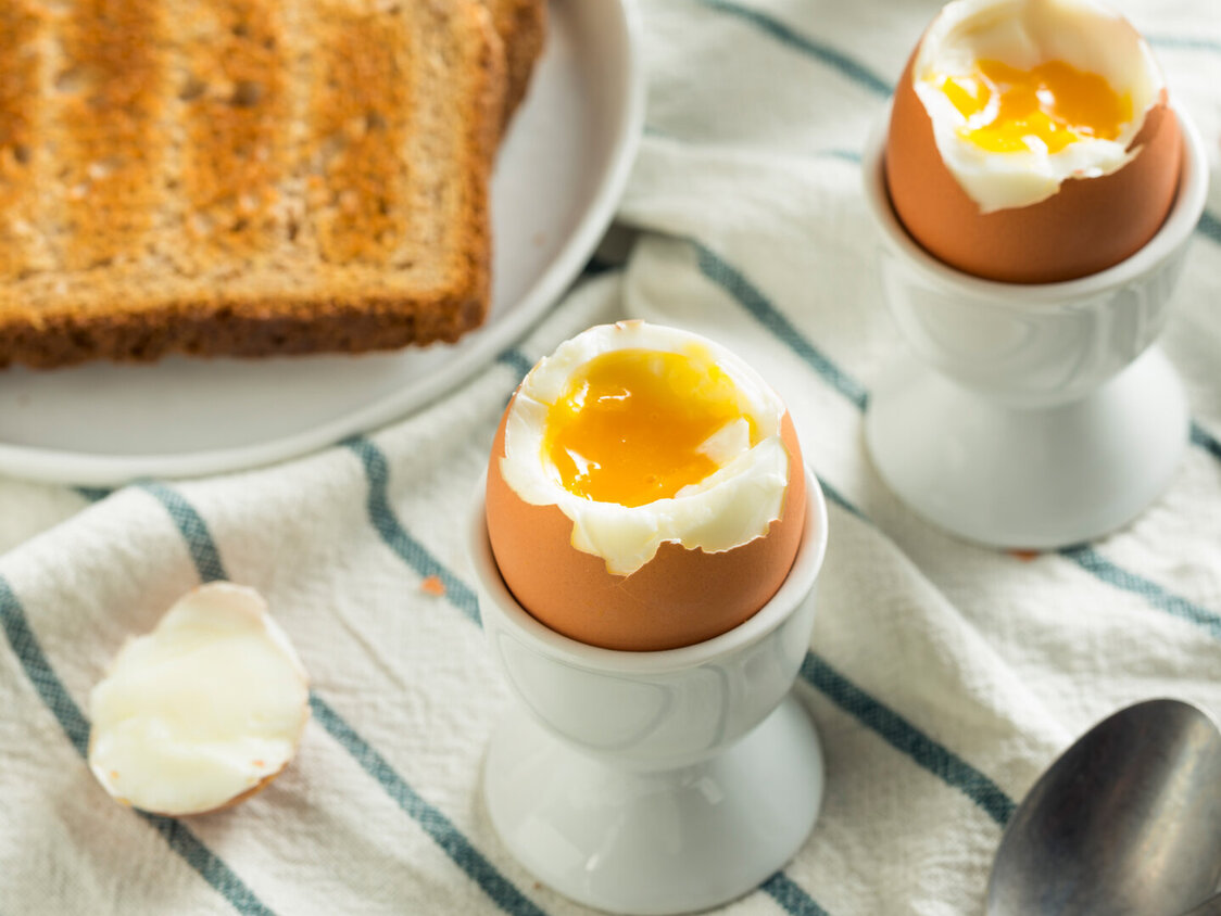 Zwei weichgekochte Eier in Eierbechern, daneben eine Scheibe Toast.