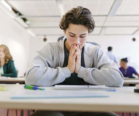 Ein Junge sitzt in der Schule am Tisch und guckt verzweifelt auf seine Unterlagen.