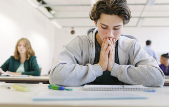 Ein Junge sitzt in der Schule am Tisch und guckt verzweifelt auf seine Unterlagen.