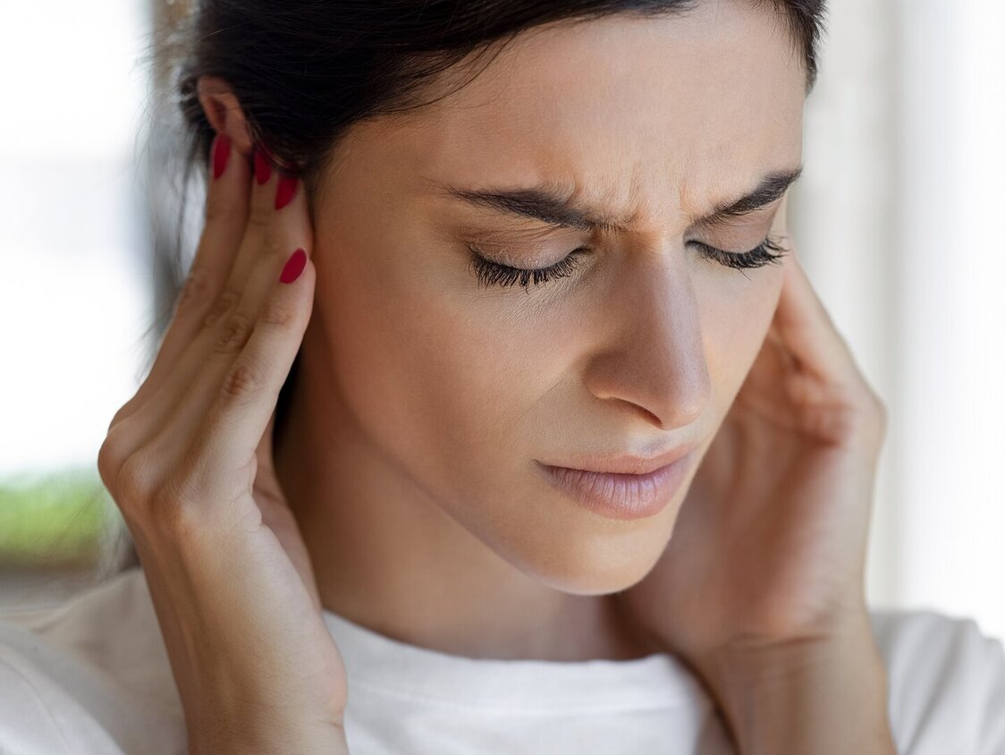 Frau hält sich mit schmerzverzerrtem Gesicht die Ohren zu.