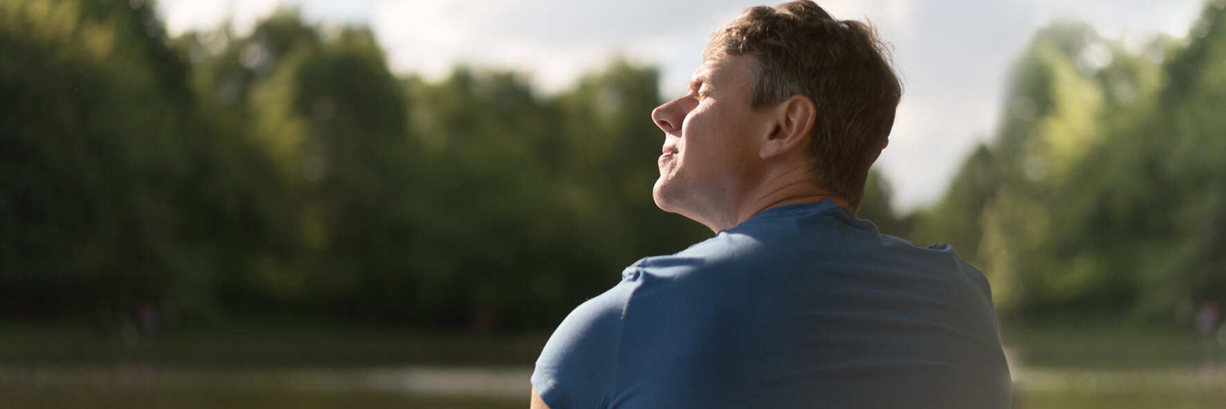 Ein Mann in blauem T-Shirt sitzt an einem See in der Sonne.