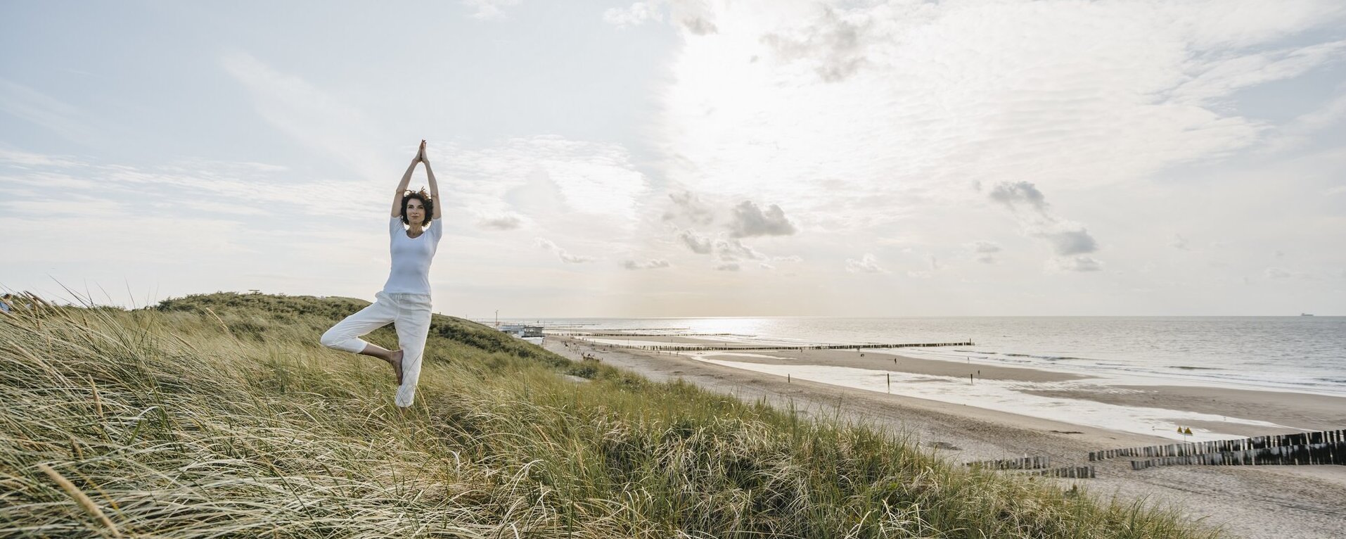 Eine Frau macht in den Dünen am Strand eine Yogaübung.