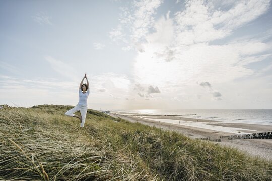 Eine Frau macht in den Dünen am Strand eine Yogaübung.