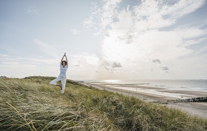 Eine Frau macht in den Dünen am Strand eine Yogaübung.