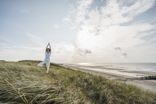 Eine Frau macht in den Dünen am Strand eine Yogaübung.
